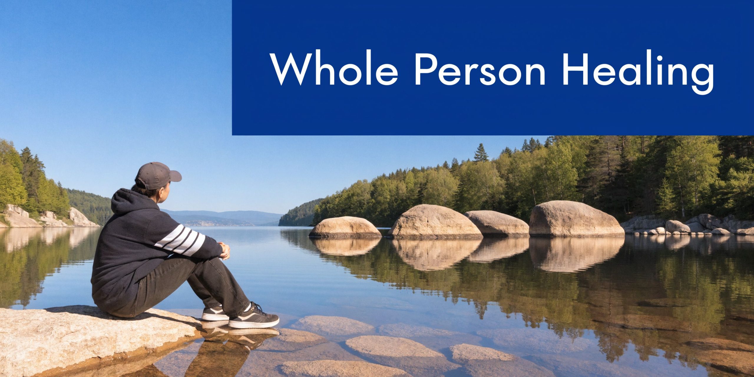 A person sitting on a rock by a calm lake reflecting on their health and healing journey.