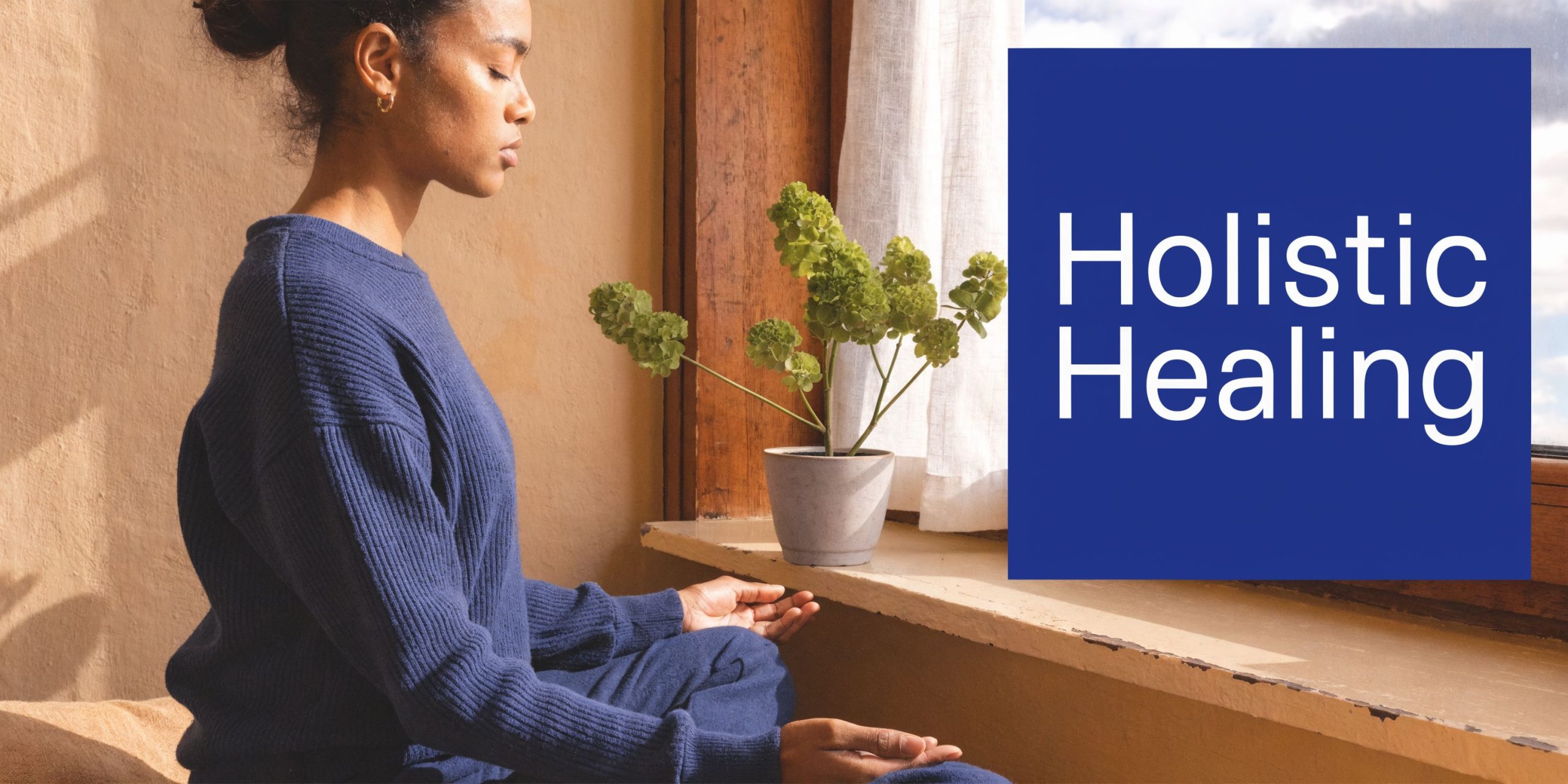 A woman in a blue sweater meditates calmly by a sunny window with a green potted plant.