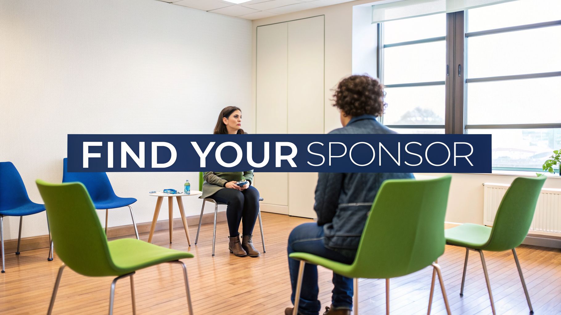 Two women seated in a bright room with chairs, engaging in a sponsor meeting or discussion.