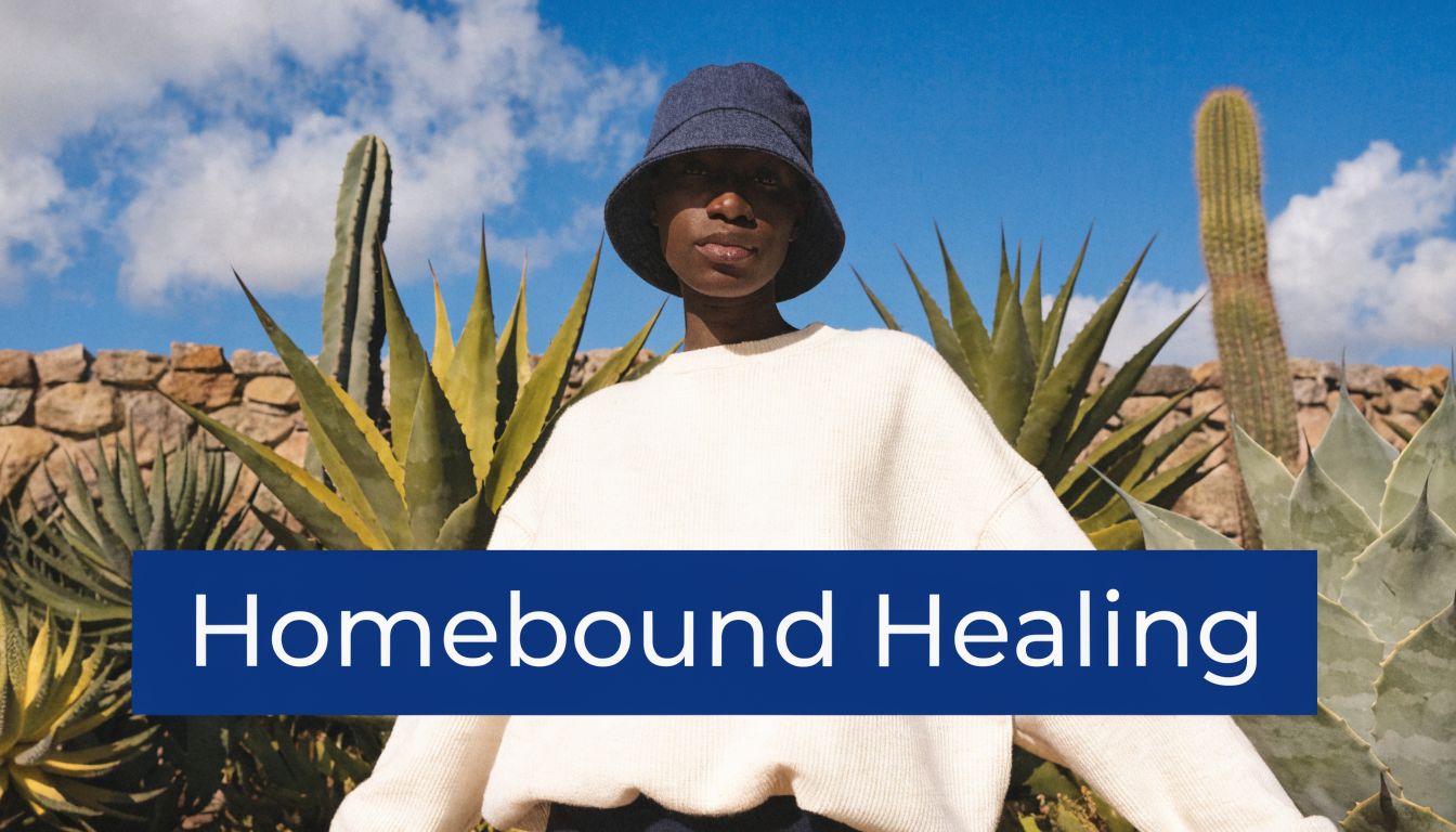 A person wearing a bucket hat and sweater standing in front of cacti and a stone wall.