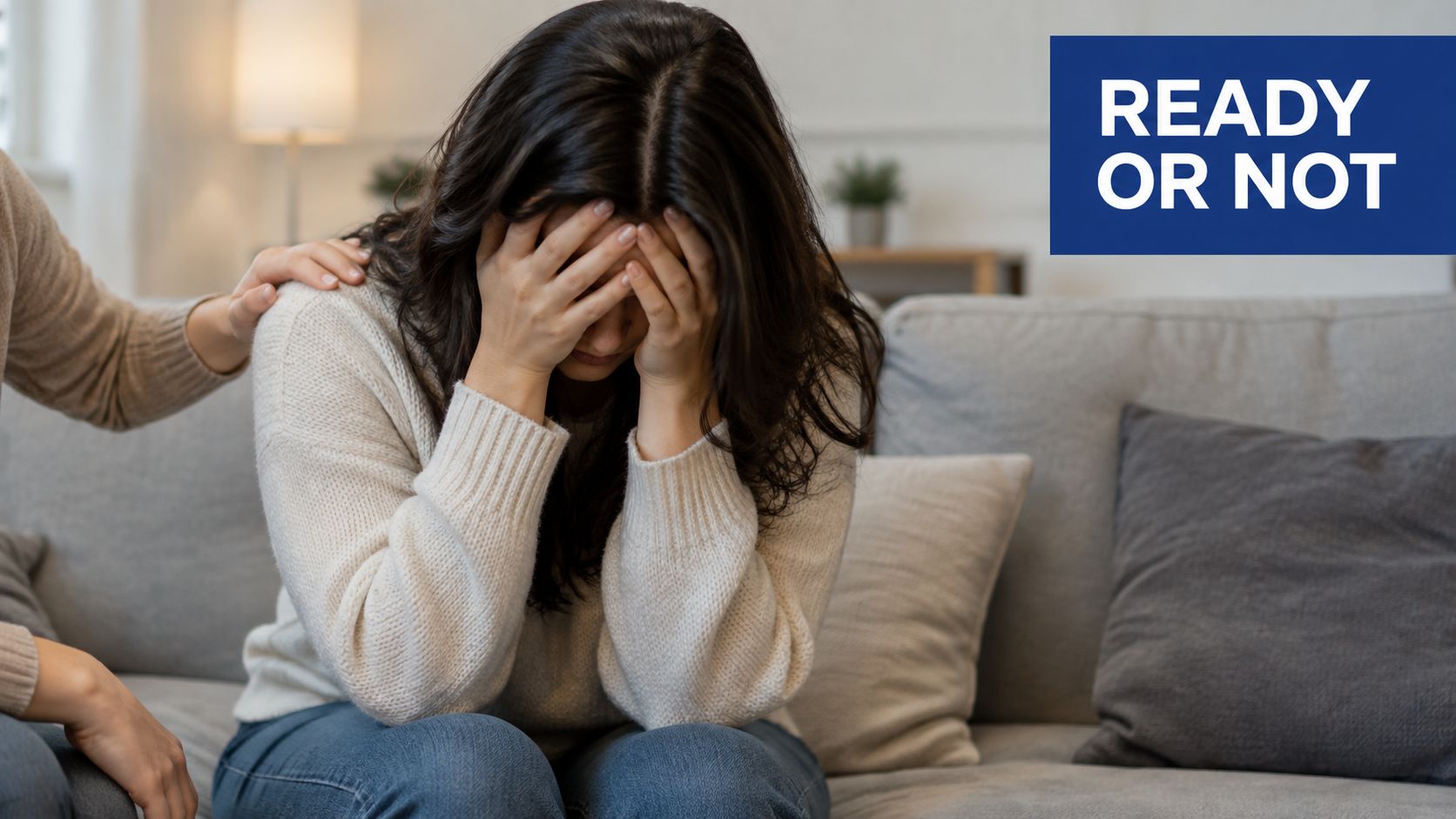A person offering comfort to a grieving woman sitting on a sofa covering her face.